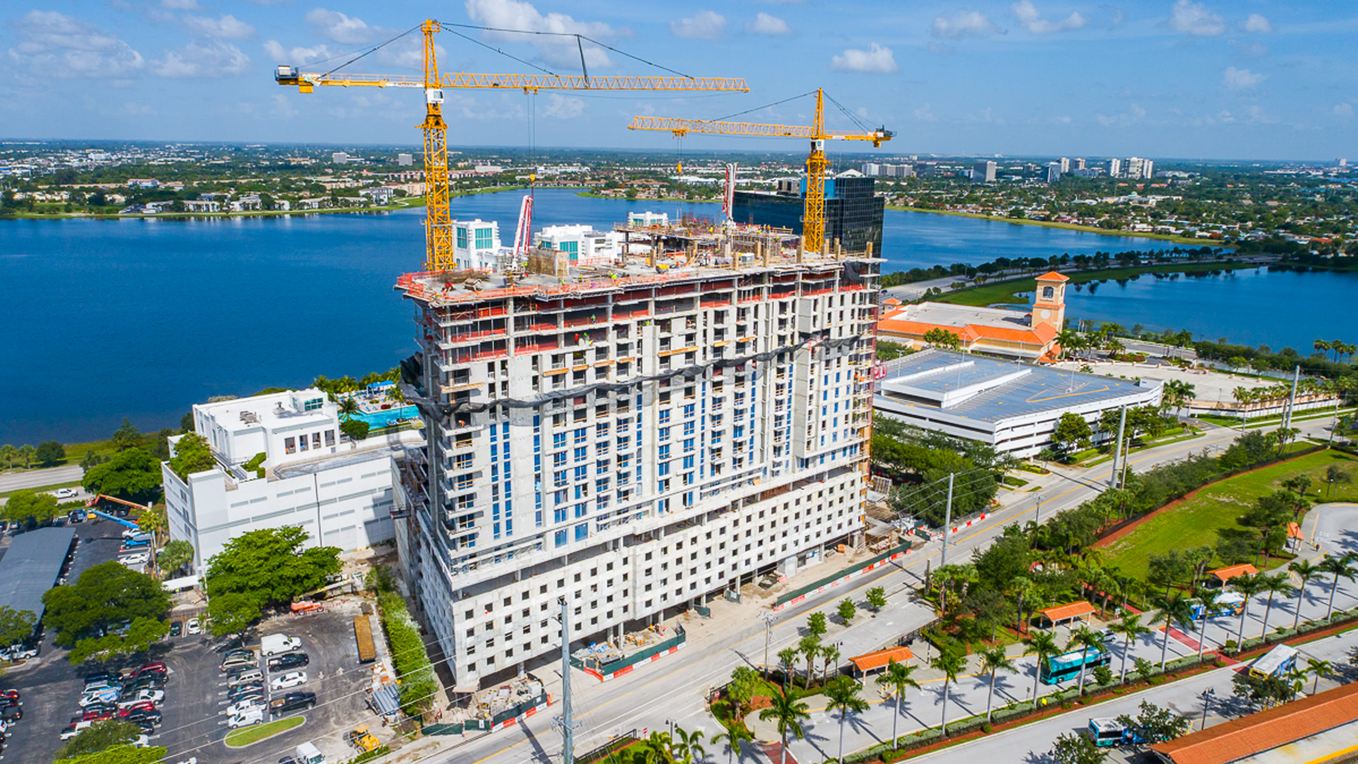 High-rise under construction beside a lake, with cranes