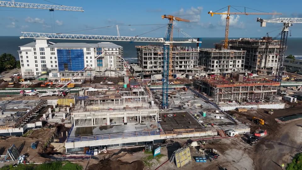 Video: sweep across a coastal construction site with tower cranes